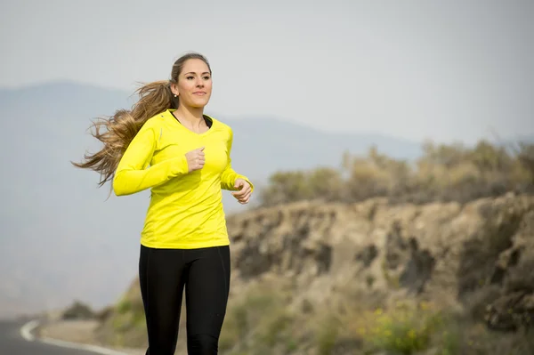Wanita muda atraktif berlari di jalan aspal dengan latar belakang pemandangan gurun pegunungan — Stok Foto