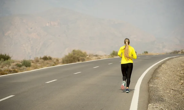 Back view of young attractive sport woman running on desert mountain asphalt road — Zdjęcie stockowe