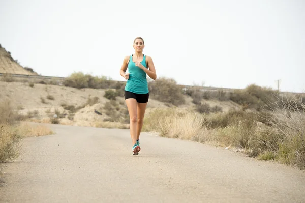 Sportlerin läuft auf Asphalt schmutzige Straße mit trockener Wüstenlandschaft Hintergrundtraining hart — Stockfoto