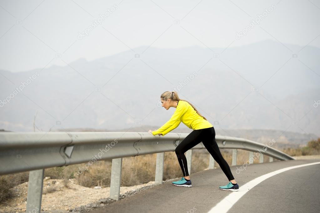 sport woman stretching leg muscle after running workout on asphalt road with dry desert landscape in hard fitness training session