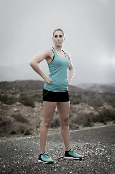 Junge attraktive Sportlerin in Jogginghose und kurzen Hosen posiert trotzig und cool in Asphaltstraße vor dem Berg — Stockfoto