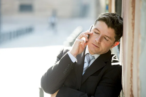 Muda menarik dan sibuk pengusaha dengan mata tertutup mengenakan jas dan dasi berbicara bisnis di telepon genggam luar ruangan — Stok Foto