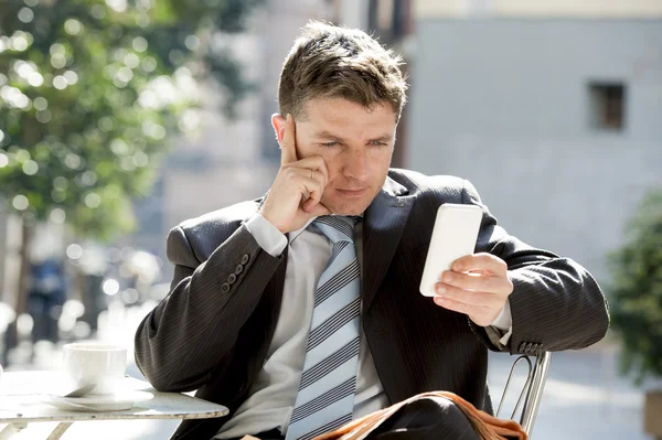 Attraente uomo d'affari seduto all'aperto in pausa caffè utilizzando il telefono cellulare cercando premuroso — Foto Stock