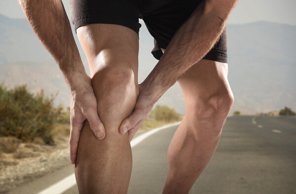 young sport man with athletic legs holding knee in pain suffering muscle injury running 
