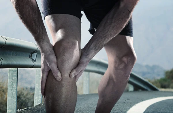 Jovem homem do esporte com pernas atléticas segurando joelho com dor sofrendo lesão muscular correndo — Fotografia de Stock