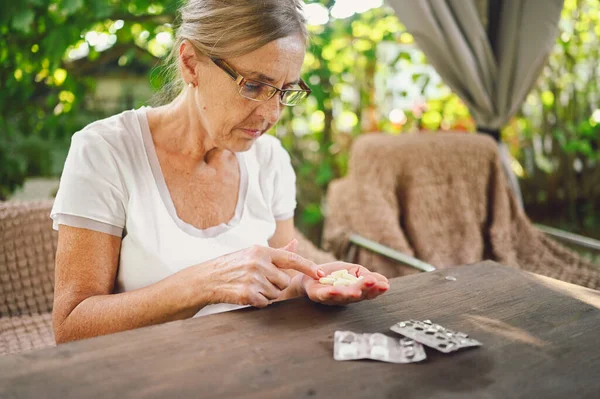 Elderly happy senior old woman in spectacles prescription glasses takes medicine drugs vitamins pills outdoors in the garden. Healthcare aged people lifestyle concept