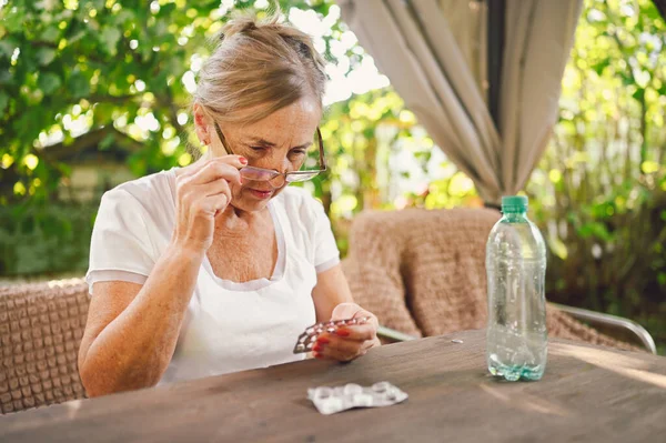 Wanita dewasa berkacamata memegang pil Membaca instruksi obat pada kemasan sebelum mengambil obat — Stok Foto