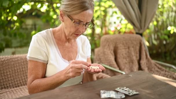 Seniorin mit Brille nimmt Vitamintabletten im Garten. Gesundheitskonzept für ältere Menschen