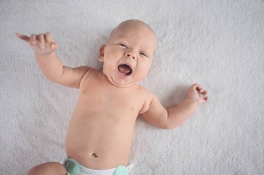 Sevimli, duygusal, gülümseyen, yeni doğmuş komik çocuk yatağın üstünde yatıyor. Bebek yüz ifadeleri. Mal paketleme şablonu. Sağlıklı çocuk, hastane kavramı ve mutlu annelik. Bebek, bebek. Çocuk odası..