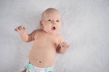 Sevimli, duygusal, gülümseyen, yeni doğmuş komik çocuk yatağın üstünde yatıyor. Bebek yüz ifadeleri. Mal paketleme şablonu. Sağlıklı çocuk, hastane kavramı ve mutlu annelik. Bebek, bebek. Çocuk odası..