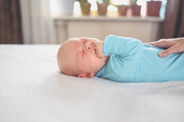 Mavi tulumlu ağlayan tatlı duygusal yeni doğmuş çocuk yatakta yatıyor. Bebek yüz ifadeleri. Bebek eşyaları paketleme şablonu. Sağlıklı çocuk, hastane kavramı ve mutlu annelik. Bebek, bebek. Çocuk odası..