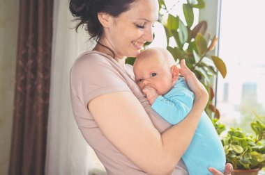 Güzel anne kucağında küçük tatlı bebeğini tutuyor. Bebek yüz ifadeleri. Evde, pencerenin yanında bir aile. Sağlıklı çocuk, hastane kavramı ve mutlu annelik. Çocuk odası..