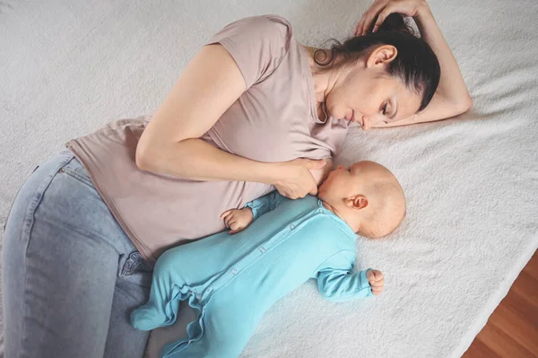 年轻的母亲躺在床上 抱着一个穿着蓝色连衣裙的可爱的新生儿 用母乳喂他 健康的孩子 医院的概念和快乐的母性 幼儿园 — 图库照片
