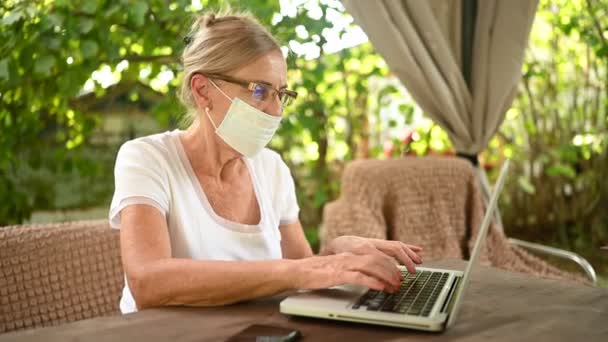 Teknik, ålderdom koncept - äldre äldre äldre kvinna tar av skyddande ansiktsmask andas hårt arbetar online med bärbar dator utomhus i trädgården. Fjärrarbete, distansutbildning — Stockvideo