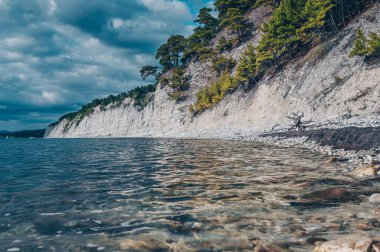 Su yüzeyinden Karadeniz kıyısına harika bir manzara. Beyaz kayalar üzerinde yeşil ağaçlar ve dramatik mavi bulutlu gökyüzü. Blue Deep - Golubaja bezdna Gelendzhik ilçesi, Krasnodar bölgesi, Rusya