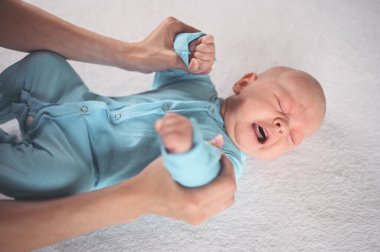 Annem duygusal açıdan komik, yeni doğmuş erkek bebeğe mavi tulum giydiriyor. Bebek eşyaları paketleme şablonu. Sağlıklı çocuk, hastane kavramı ve mutlu annelik. Bebek, bebek. Çocuk odası..