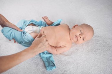 Annem duygusal açıdan komik, yeni doğmuş erkek bebeğe mavi tulum giydiriyor. Bebek eşyaları paketleme şablonu. Bebek bezi takan sağlıklı bir çocuk, hastane konsepti ve mutlu annelik. Bebek, bebek. Çocuk odası..