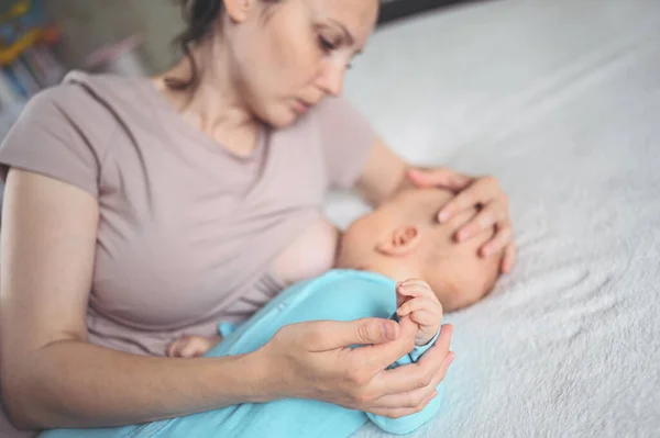 어머니는 침대에 점프수트를 태어난 귀여운 아기와 젖으로 아기를 껴안고 먹인다 — 스톡 사진