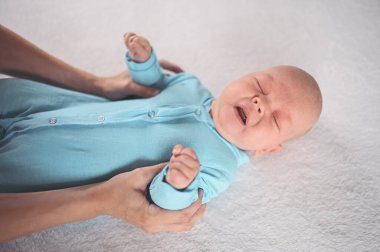 Annem duygusal açıdan komik, yeni doğmuş erkek bebeğe mavi tulum giydiriyor. Bebek eşyaları paketleme şablonu. Sağlıklı çocuk, hastane kavramı ve mutlu annelik. Bebek, bebek. Çocuk odası..