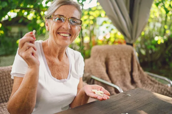 Wanita tua berkacamata meminum pil vitamin di luar ruangan di kebun. Kesehatan orang-orang usia konsep — Stok Foto