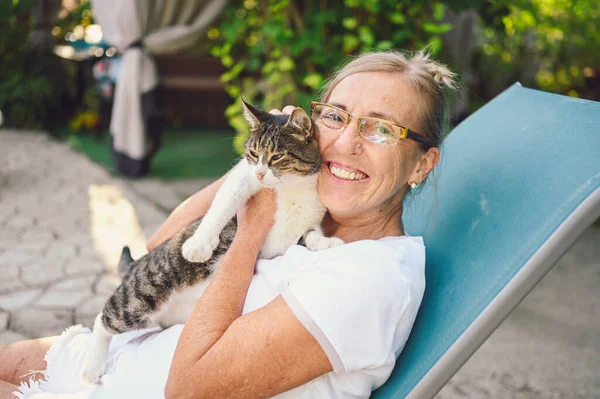ผู้หญิงวัยรุ่นที่มีความสุขยิ้มในแว่นตา ผ่อนคลายในสวนฤดูร้อน กอดแมวทับบี้ในบ้าน — ภาพถ่ายสต็อก