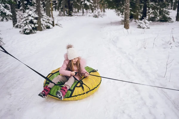 雪に覆われた白い冬の屋外で楽しい乗り物インフレータブル雪チューブを持つピンクの暖かい耳の中の小さなかわいい女の子 家族スポーツ休暇活動 — ストック写真
