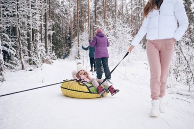 Mutlu anne ve küçük sevimli kız pembe, sıcak, yürüyüş kıyafetleri içinde dışarıda kar ormanlarında şişirilebilir kar tüpleriyle geziyorlar. Aile spor tatili aktiviteleri