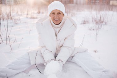 Beyaz, sıcak, güneşli kışın açık havada karla oynayan yaşlı, mutlu, olgun bir kadın. Emekli sağlıklı insanlar tatil, kış aktiviteleri, aktif yaşam tarzı konsepti
