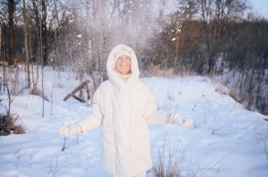Beyaz, sıcak, güneşli kışın açık havada karla oynayan yaşlı, mutlu, olgun bir kadın. Emekli sağlıklı insanlar tatil, kış aktiviteleri, aktif yaşam tarzı konsepti