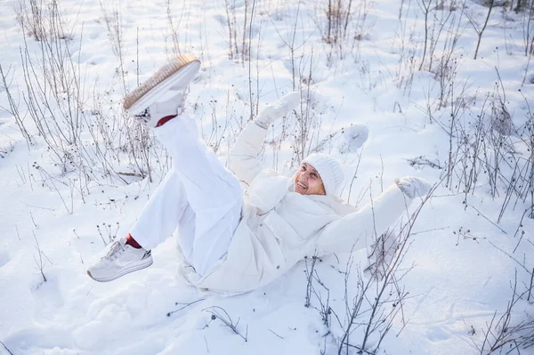 Happy elderly senior mature woman in white warm outwear playing with snow in sunny winter outdoors. Retired healthy people holiday vacation winter activities, active lifestyle concept