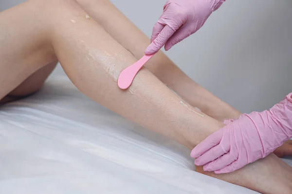 Laser epilation and cosmetology in beauty salon, spa concept. Preparation for the procedure of laser hair removal. Application of gel, disposable spatula. Beautiful smooth female legs