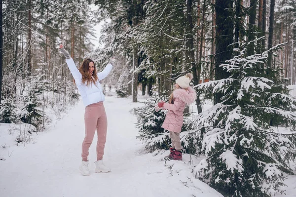 雪に覆われた白い冬の針葉樹林で楽しむ雪合戦を屋外でスプルースの森とピンクの暖かい外耳道で幸せな母親と小さなかわいい女の子 家族スポーツ休暇活動 — ストック写真
