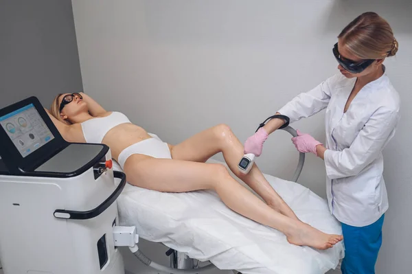 Istilah laser dan kosmetologi di salon kecantikan. Prosedur pengangkatan rambut. Laser epilasi, kosmetologi, spa, dan rambut menghilangkan konsep. Wanita pirang cantik sedang memotong rambut dengan kaki.. — Stok Foto