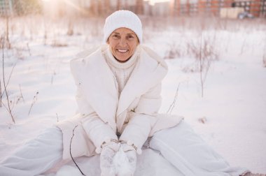 Beyaz, sıcak, güneşli kışın açık havada karla oynayan yaşlı, mutlu, olgun bir kadın. Emekli sağlıklı insanlar tatil, kış aktiviteleri, aktif yaşam tarzı konsepti