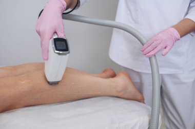 Güzellik salonunda lazer epilasyonu ve kozmetoloji. Saç çıkarma prosedürü. Lazer epilasyonu, kozmetoloji, spa ve saç temizleme konsepti. Güzel sarışın kadın saçlarını bacaklarından ayırıyor.