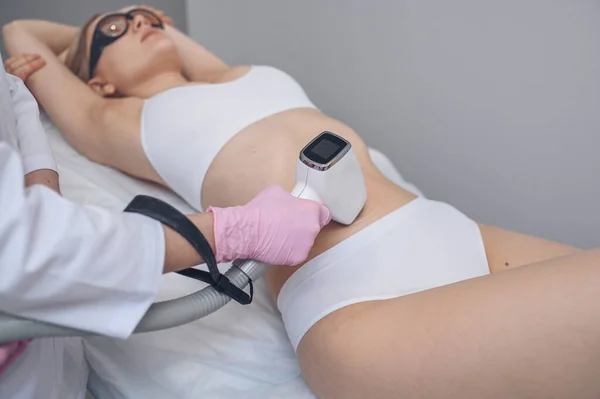 Laser epilation and cosmetology in beauty salon. Hair removal procedure. Laser epilation, cosmetology, spa, and hair removal concept. Beautiful blonde woman getting hair removing on stomach