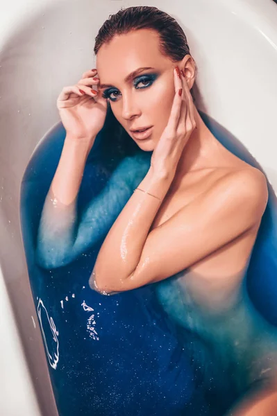 漂亮的年轻女子穿着时髦的衣服 在一个充满彩色蓝色宇宙浴池炸弹水的复古浴缸里摆出沐浴姿势 温泉美容院的概念 身体和皮肤护理 — 图库照片