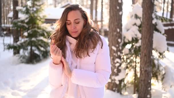 겨울 햇살 이 따사 로운 흰옷을 입은 아름다운 젊은 여인 이 눈덮인 푸른 가문비나무들 이 배경에 있는 시골 목조 주택의 뒤 뜰에 앉아 있는 눈내리는 추운 사진. — 비디오