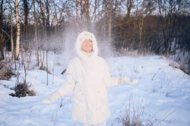 Beyaz, sıcak, güneşli kışın açık havada karla oynayan yaşlı, mutlu, olgun bir kadın. Emekli sağlıklı insanlar tatil, kış aktiviteleri, aktif yaşam tarzı konsepti