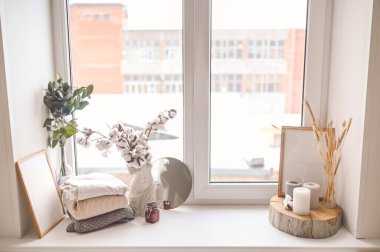 Samimi, hayat kadınsı sahne pastel renkleri. Kadın stili pencere pervazı minimalist kompozisyonu. Boş poster çerçevesi, zarif aksesuar aynası katlanmış kazaklar, mumlar, kuru pamuk çiçekler.