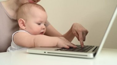 Küçük bebek portresini kapat. Komik yüz ifadesi. Annesinin kucağında oturup dizüstü bilgisayar çalışıyor. Genç anne evde bilgisayarla çalışıyor. Merkez ofis, ebeveynlik. Uzak çalışma, uzak eğitim. .