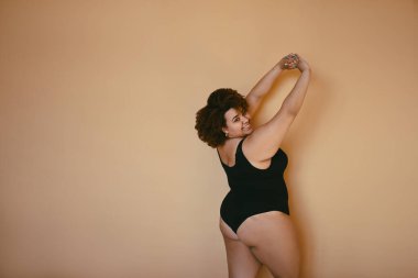 Güzel, kıvrımlı, Afrikalı, siyah, siyah bir kadın saçı var, bej kahverengi arka planda poz veriyor, izole edilmiş, vücut kusuru, vücut kabulü, vücut pozitifliği ve çeşitlilik kavramı. Kopyalama alanı.