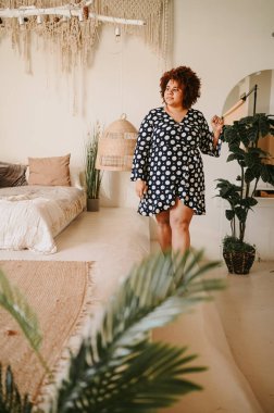 Kıvrımlı, Afrikalı, siyah, siyah, siyah, siyah saçlı, siyah saçlı, ev bitkileriyle çevrili, çevre dostu, samimi yatak odası iç tasarımı. Vücut kusuru, beden kabulü, vücut pozitifliği ve çeşitlilik kavramı