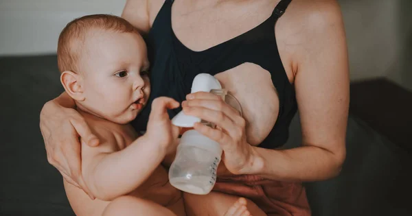 Jovem mãe com recém-nascido bonito bebê menino nu, segurando-o nos braços, usando abraço bomba de mama e amamenta com leite materno. Criança saudável, conceito de hospital e maternidade feliz. Berçário. — Fotografia de Stock