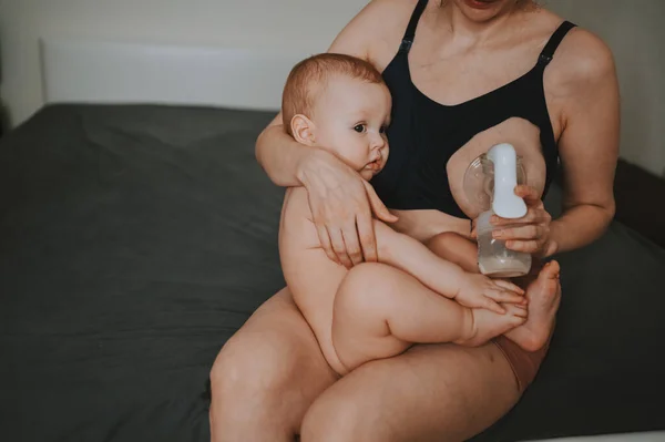 Young mother with newborn cute infant naked baby boy, holding him on arms, using breast pump hugging and breastfeeds with breast milk. Healthy child, concept of hospital and happy motherhood. Nursery. Stock Image