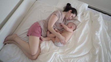 Yeni doğmuş tatlı bebek hiperaktif bebekle yatakta yatmaktan yorgun bir anne onu kollarına alıp anne sütüyle emziriyor. Sağlıklı çocuk, hastane kavramı ve mutlu annelik. Çocuk odası.