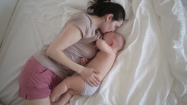 Giovane madre sdraiata con neonato carino bambino nudo sul letto, tenendolo sulle braccia, abbracciandolo e allattandolo con latte materno. Bambino sano, concetto di ospedale e maternità felice. Vivaio — Video Stock