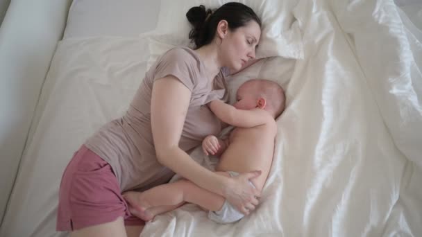 Trött mamma sover med nyfödda söta spädbarn naken pojke på sängen, håller honom på armar, kramar och ammar med bröstmjölk. Friska barn, begreppet sjukhus och lycklig moderskap. Plantskola — Stockvideo