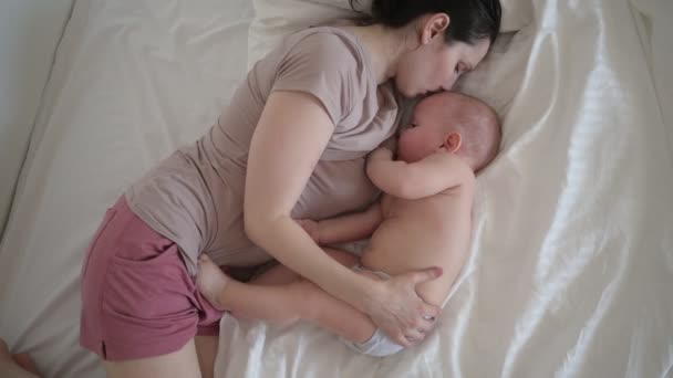 Giovane madre sdraiata con neonato carino bambino nudo sul letto, tenendolo sulle braccia, abbracciandolo e allattandolo con latte materno. Bambino sano, concetto di ospedale e maternità felice. Vivaio — Video Stock