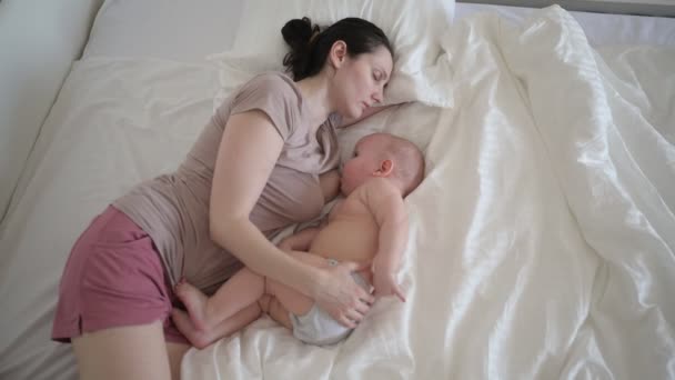 疲惫的母亲在床上与新生儿可爱的赤身裸体男婴睡在一起，抱着他，抱着他，用母乳喂奶。健康的孩子，医院的概念和快乐的母性。幼儿园 — 图库视频影像